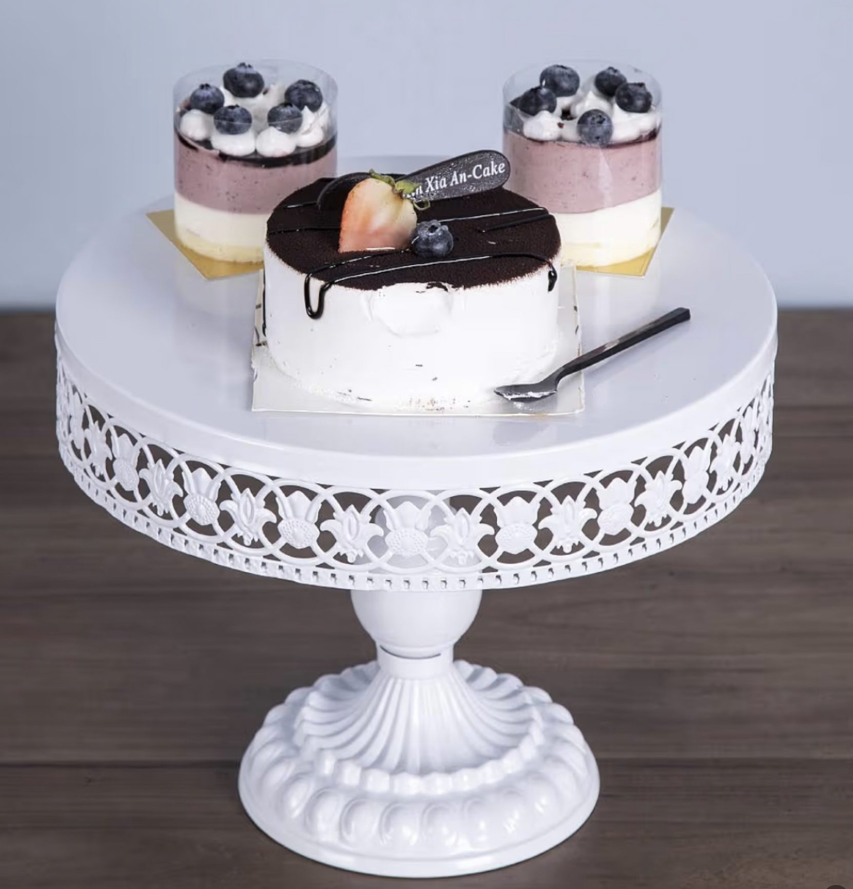 A beautifully decorated cake stand displaying a chocolate cake topped with fruit and two desserts with blueberries, showcasing an elegant design.